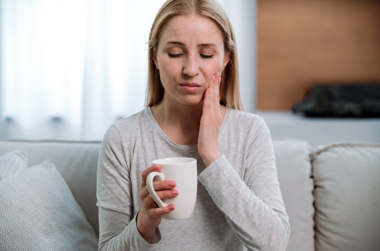 Woman experiencing tooth pain while drinking a hot or cold beverage from a cup.